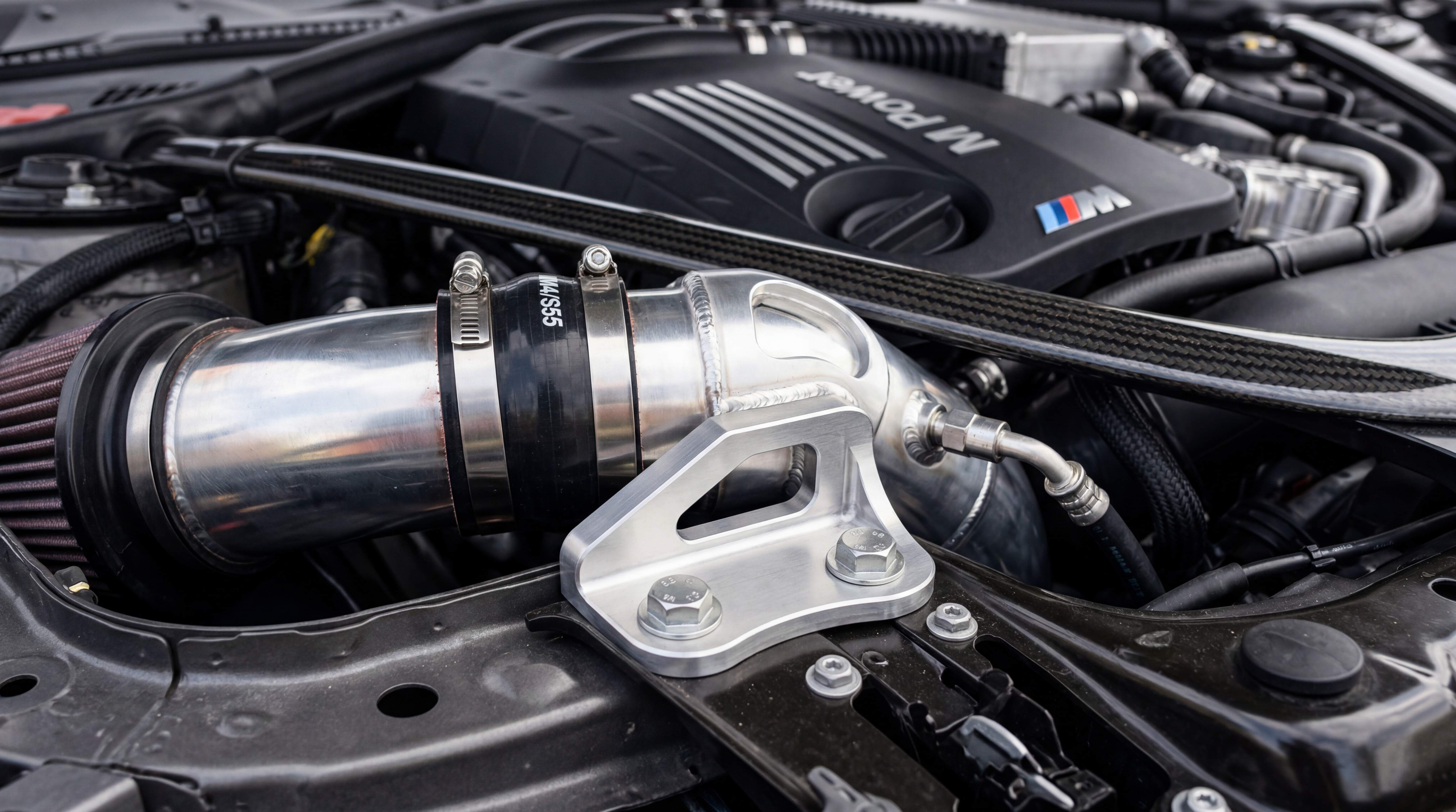 Close-up of an intake pipe bracket and mounting support securing an aluminum intake pipe in the engine bay